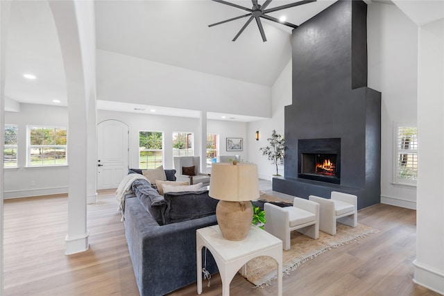 living room featuring a large fireplace, light hardwood / wood-style flooring, high vaulted ceiling, and a healthy amount of sunlight