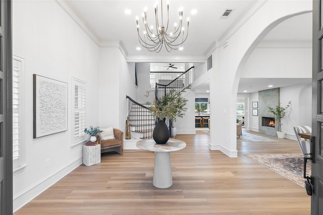 foyer entrance with a high ceiling, ceiling fan with notable chandelier, crown molding, a fireplace, and light hardwood / wood-style floors