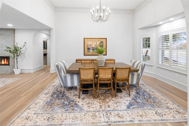 dining space featuring a large fireplace, hardwood / wood-style floors, an inviting chandelier, and ornamental molding