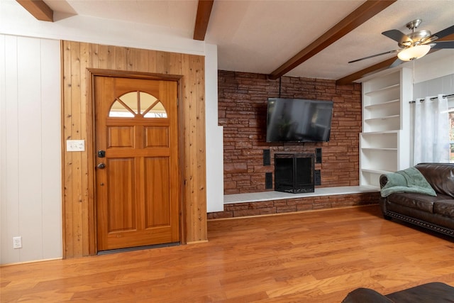 living room with hardwood / wood-style floors, built in shelves, a fireplace, wooden walls, and ceiling fan