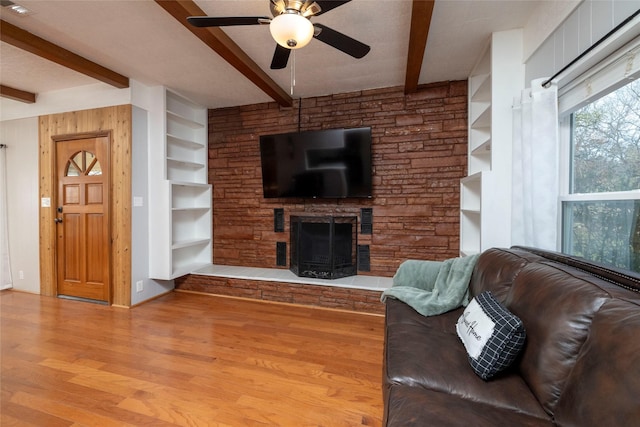 living room with ceiling fan, beamed ceiling, hardwood / wood-style flooring, built in features, and a stone fireplace