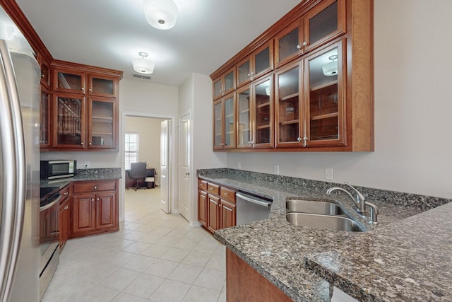 kitchen with sink, light tile patterned floors, dark stone countertops, stainless steel appliances, and built in desk