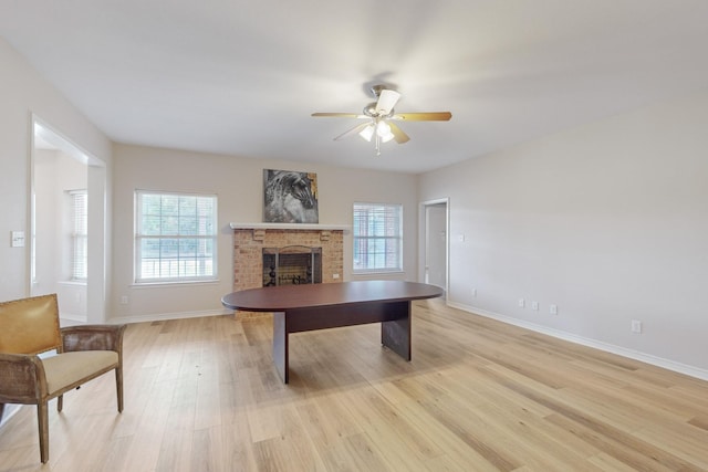 unfurnished office with ceiling fan, a brick fireplace, and light hardwood / wood-style flooring