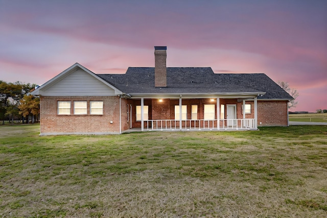 back house at dusk with covered porch and a lawn