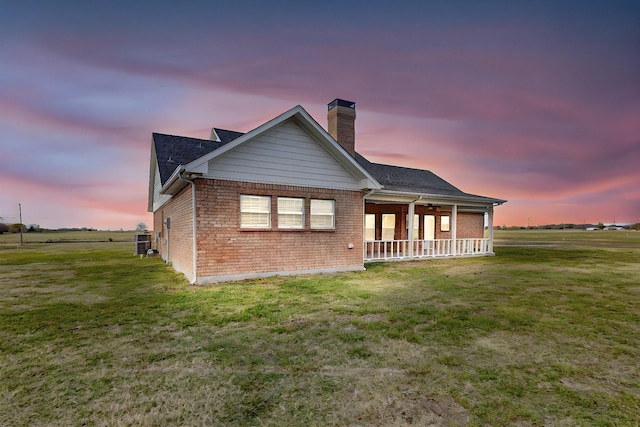 back house at dusk featuring a porch and a lawn