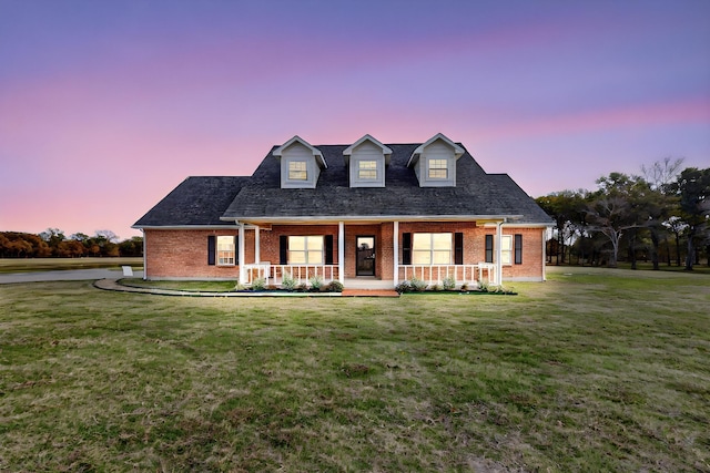 cape cod house with a lawn and covered porch