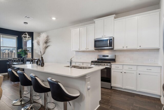 kitchen featuring appliances with stainless steel finishes, sink, pendant lighting, white cabinets, and dark hardwood / wood-style floors