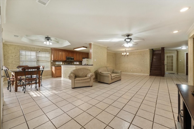 tiled living room with ceiling fan with notable chandelier, a raised ceiling, and ornamental molding