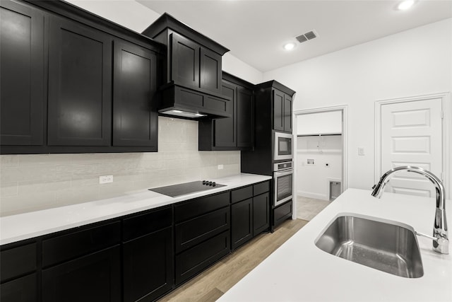 kitchen featuring custom exhaust hood, sink, light wood-type flooring, oven, and black electric cooktop