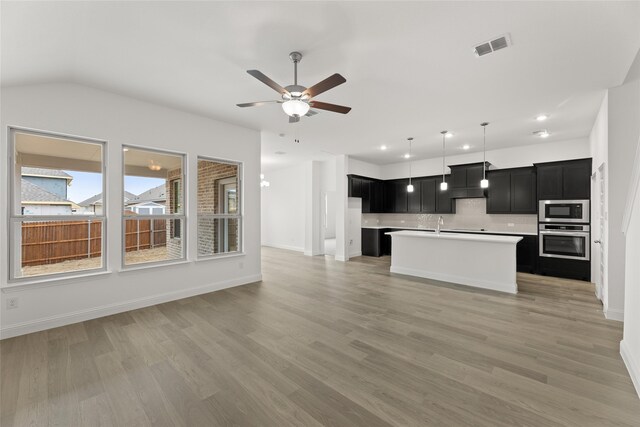 kitchen with decorative light fixtures, oven, a center island with sink, and built in microwave