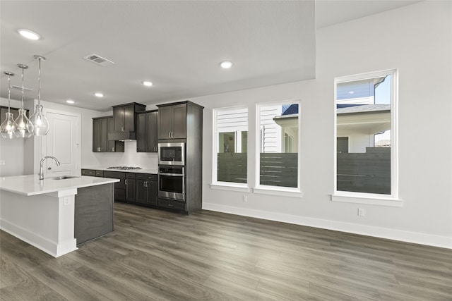 kitchen with dark hardwood / wood-style flooring, stainless steel appliances, a kitchen island with sink, sink, and hanging light fixtures