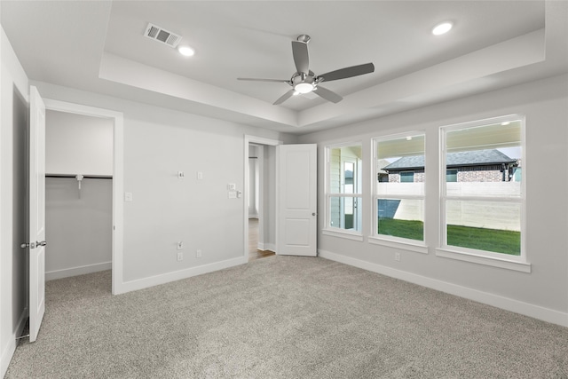 unfurnished bedroom with a walk in closet, ceiling fan, a tray ceiling, carpet floors, and a closet