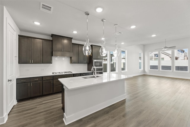 kitchen with pendant lighting, a kitchen island with sink, sink, dark brown cabinetry, and stainless steel appliances