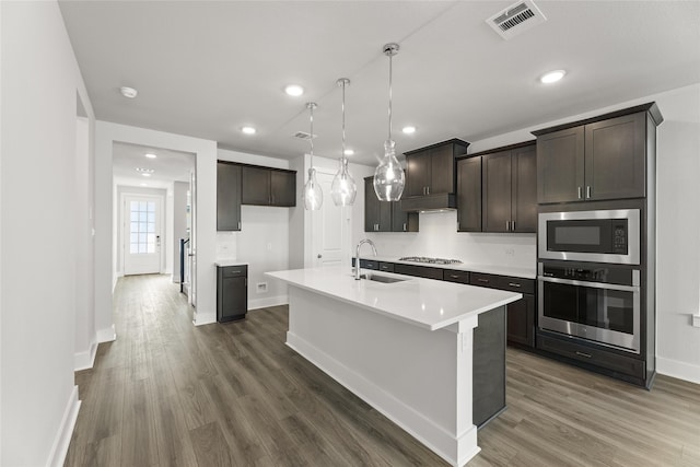 kitchen featuring sink, stainless steel appliances, dark hardwood / wood-style floors, decorative light fixtures, and a center island with sink