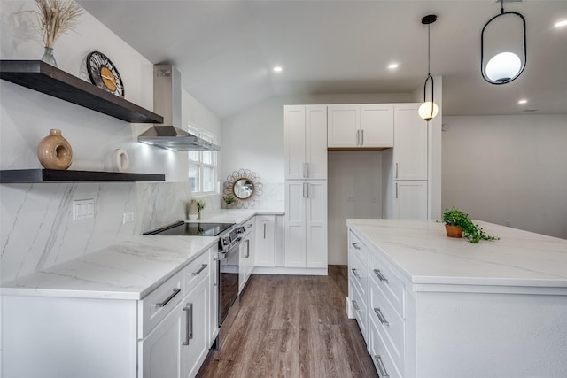 kitchen featuring wall chimney range hood, white cabinets, and decorative light fixtures