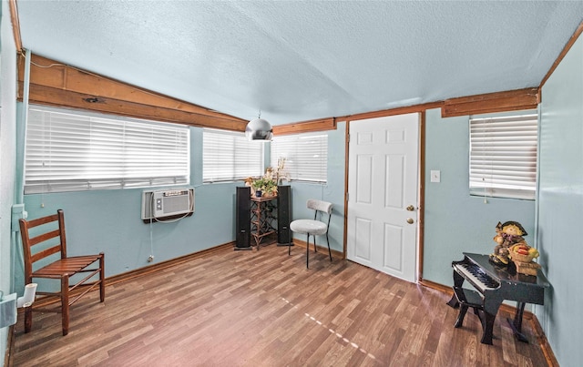 living area featuring lofted ceiling, a textured ceiling, wood finished floors, and a wall mounted air conditioner