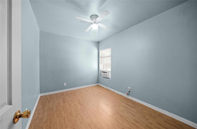 spare room featuring a ceiling fan, light wood-type flooring, cooling unit, and baseboards