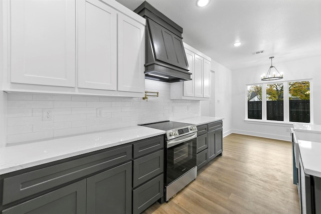 kitchen with stainless steel electric range oven, tasteful backsplash, a notable chandelier, white cabinets, and light wood-type flooring