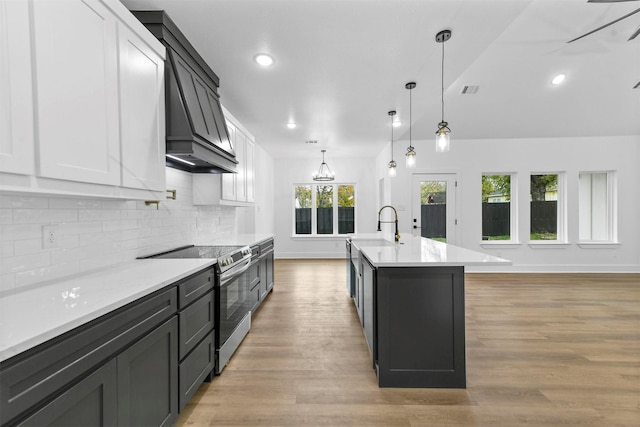 kitchen with light wood-type flooring, decorative light fixtures, stainless steel electric stove, and an island with sink