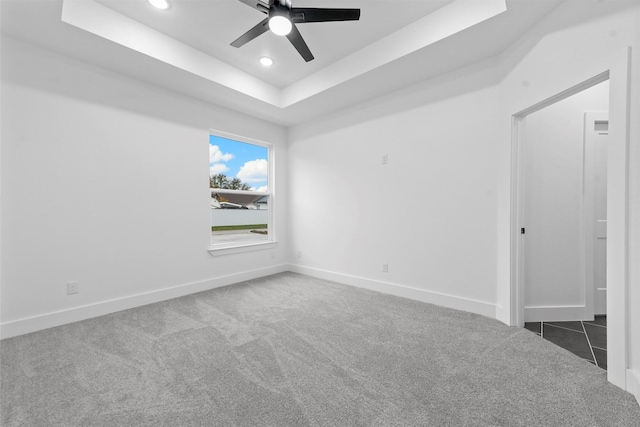 spare room featuring dark colored carpet, ceiling fan, and a raised ceiling