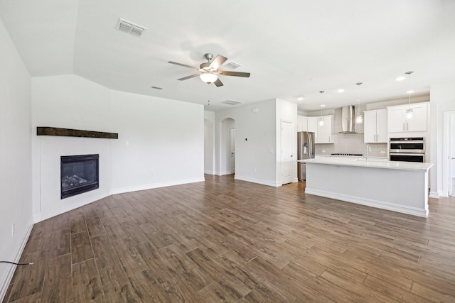 unfurnished living room featuring dark wood-type flooring, visible vents, a ceiling fan, and a glass covered fireplace