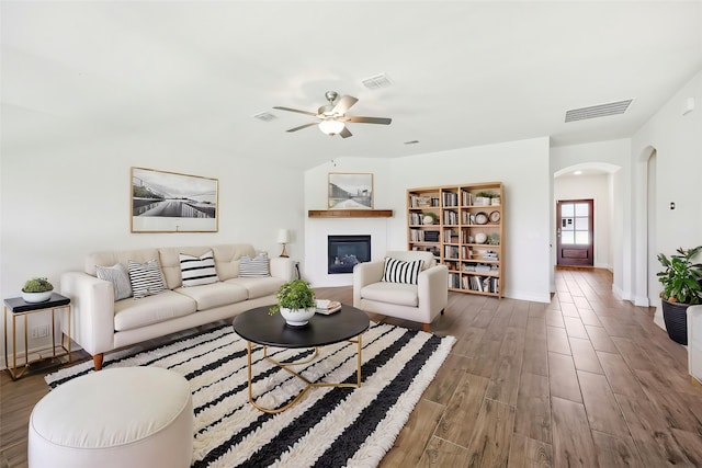 living area with a glass covered fireplace, arched walkways, visible vents, and wood finished floors