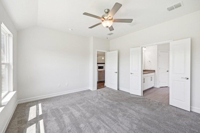 unfurnished bedroom featuring ensuite bathroom, carpet, visible vents, lofted ceiling, and baseboards