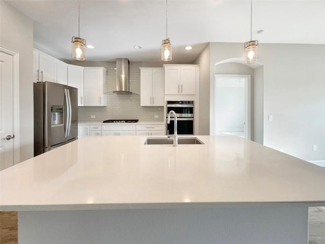 kitchen featuring white cabinetry, wall chimney range hood, an island with sink, and appliances with stainless steel finishes