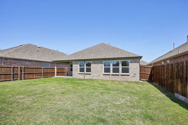 back of property featuring a shingled roof, brick siding, a fenced backyard, and a lawn