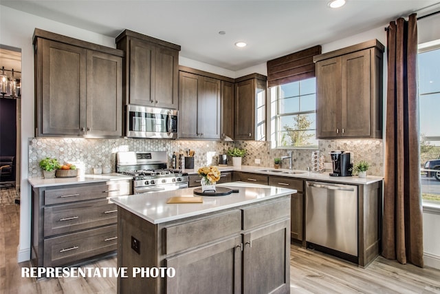 kitchen with sink, a center island, dark brown cabinets, appliances with stainless steel finishes, and light wood-type flooring