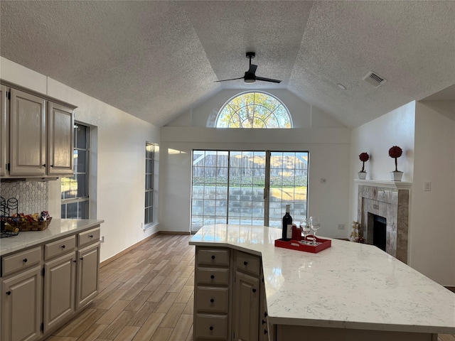 kitchen with ceiling fan, a kitchen island, vaulted ceiling, and light hardwood / wood-style flooring