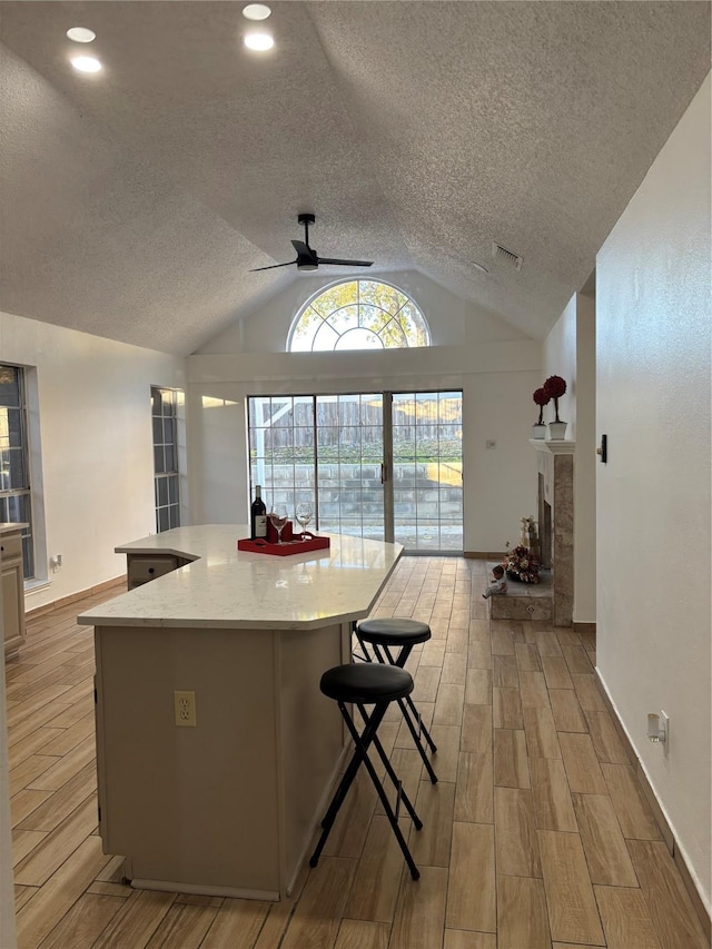 kitchen with a textured ceiling, ceiling fan, a tile fireplace, light hardwood / wood-style floors, and lofted ceiling