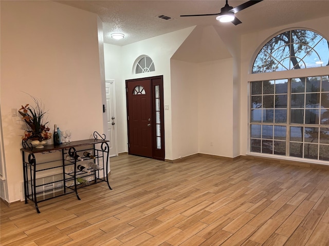 foyer entrance with ceiling fan, light hardwood / wood-style floors, a textured ceiling, and a towering ceiling