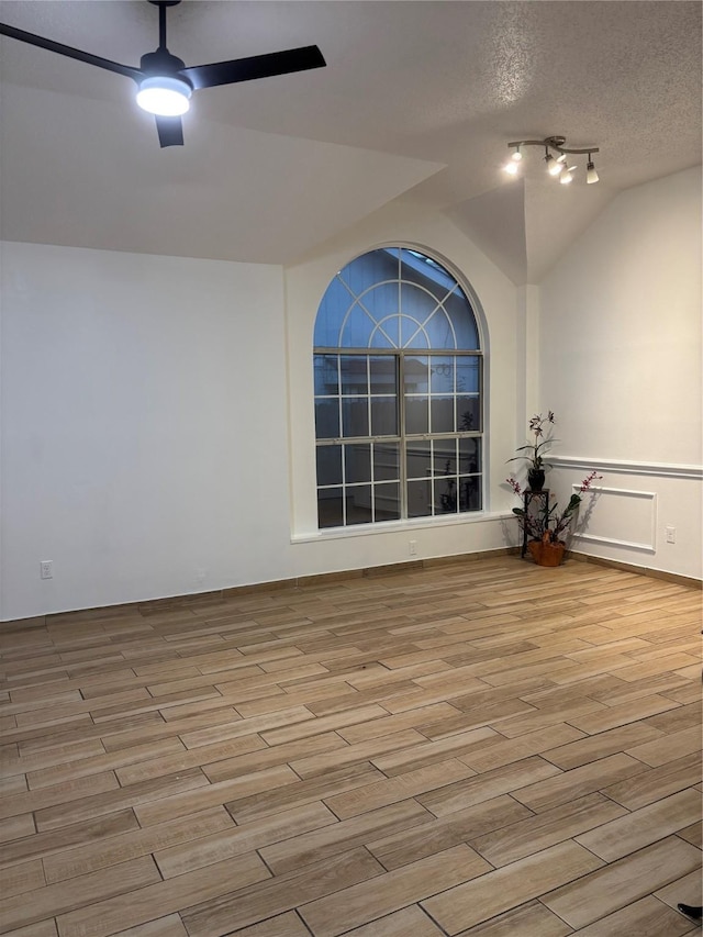 empty room featuring a textured ceiling, ceiling fan, vaulted ceiling, and light wood-type flooring