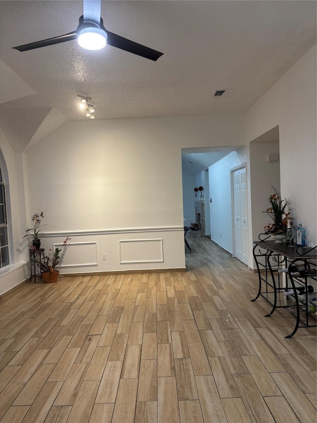 empty room with a textured ceiling, light hardwood / wood-style floors, vaulted ceiling, and ceiling fan