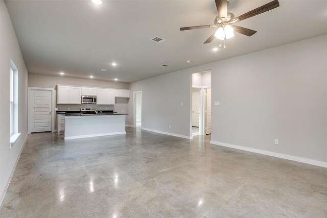 kitchen with dark stone countertops, a center island with sink, sink, stainless steel appliances, and white cabinets