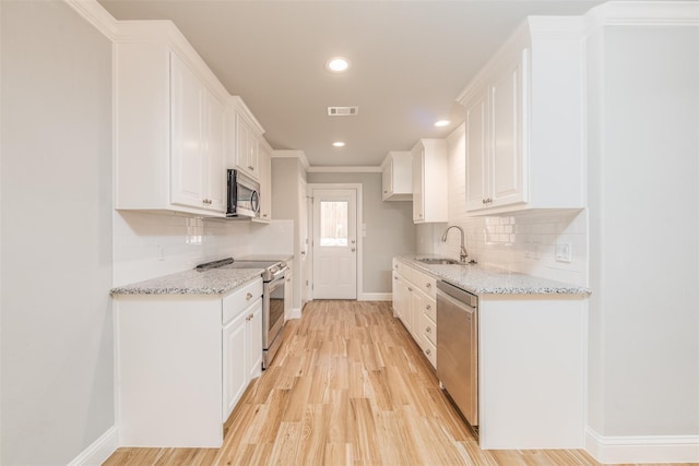 kitchen with light stone countertops, white cabinetry, light wood-type flooring, and appliances with stainless steel finishes