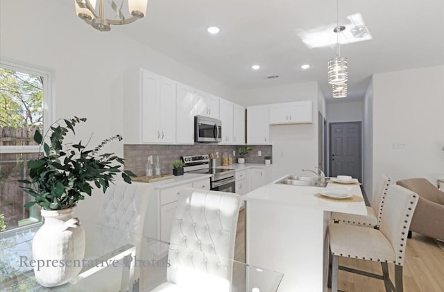 kitchen featuring decorative backsplash, stainless steel appliances, pendant lighting, white cabinets, and light hardwood / wood-style floors