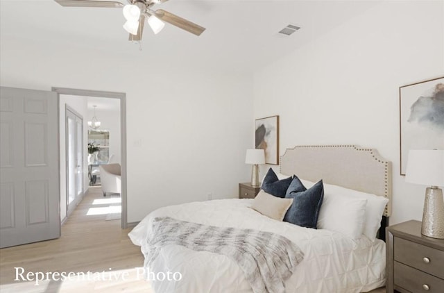 bedroom with ceiling fan with notable chandelier and light wood-type flooring