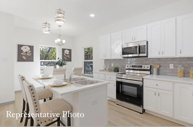 kitchen featuring sink, decorative light fixtures, a center island with sink, stainless steel appliances, and white cabinets