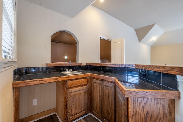 kitchen with kitchen peninsula, hardwood / wood-style floors, vaulted ceiling, and sink