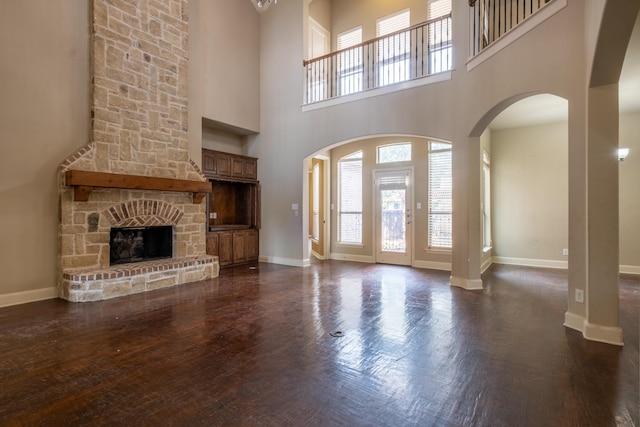 unfurnished living room featuring a stone fireplace, a towering ceiling, and dark hardwood / wood-style floors