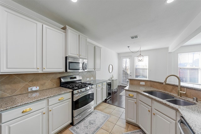 kitchen featuring pendant lighting, sink, appliances with stainless steel finishes, light hardwood / wood-style floors, and white cabinetry