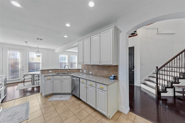 kitchen with sink, stainless steel dishwasher, light stone countertops, light hardwood / wood-style floors, and kitchen peninsula