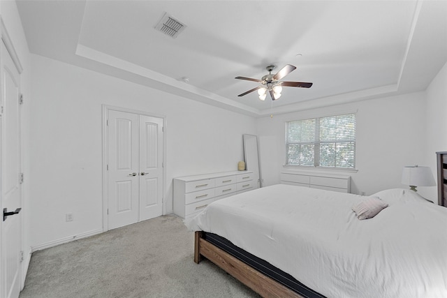 carpeted bedroom with a tray ceiling, ceiling fan, and a closet