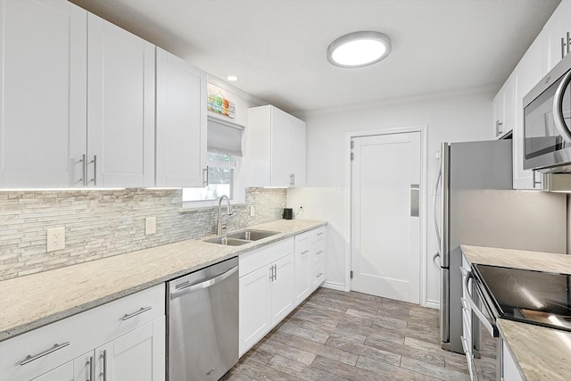 kitchen with appliances with stainless steel finishes, white cabinetry, sink, decorative backsplash, and light stone counters