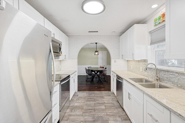 kitchen with pendant lighting, sink, appliances with stainless steel finishes, white cabinetry, and light stone countertops