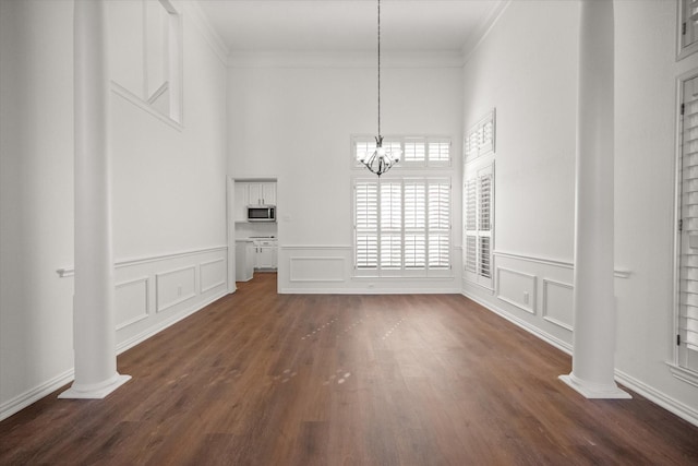 unfurnished dining area with an inviting chandelier, ornamental molding, dark wood-type flooring, and ornate columns