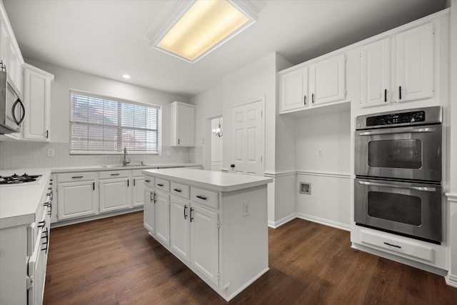 kitchen featuring appliances with stainless steel finishes, white cabinetry, sink, backsplash, and a center island