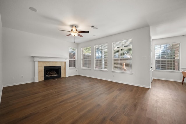 unfurnished living room featuring ceiling fan, dark hardwood / wood-style flooring, a tile fireplace, and a wealth of natural light